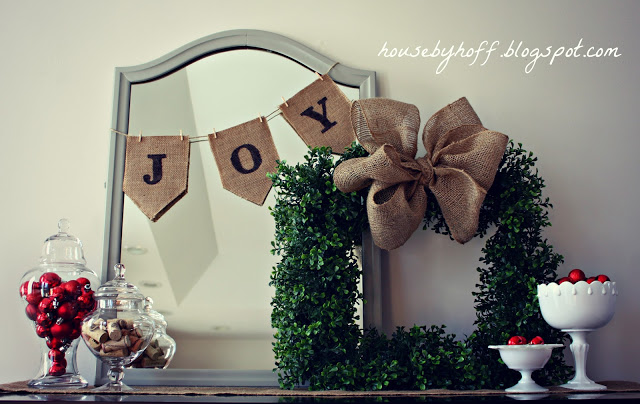 A mirror with a banner that says joy.    The boxwood wreath with a burlap bow and jars filled with candies on the mantel.