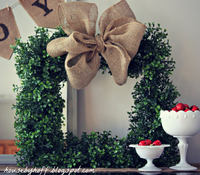 Green boxwood wreath with a burlap bow on the mantel.