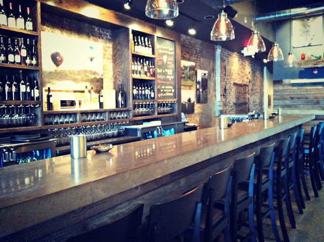 The inside of a bar with wooden chairs and pendant lights above the bar.