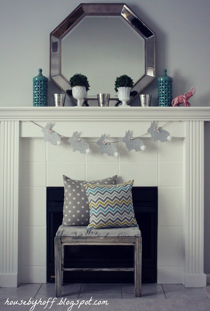 The fireplace mantel with a small bench in front of it, a mirror on the mantel and an Easter bunny garland strung from end to end.