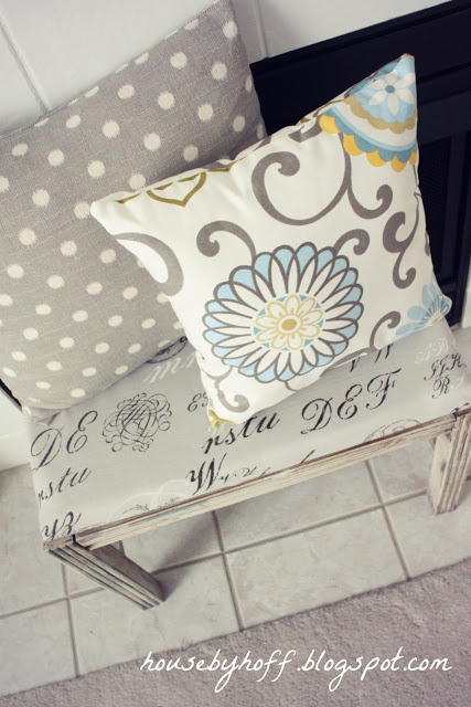 A cute bench in front of the fireplace with throw pillows on it.