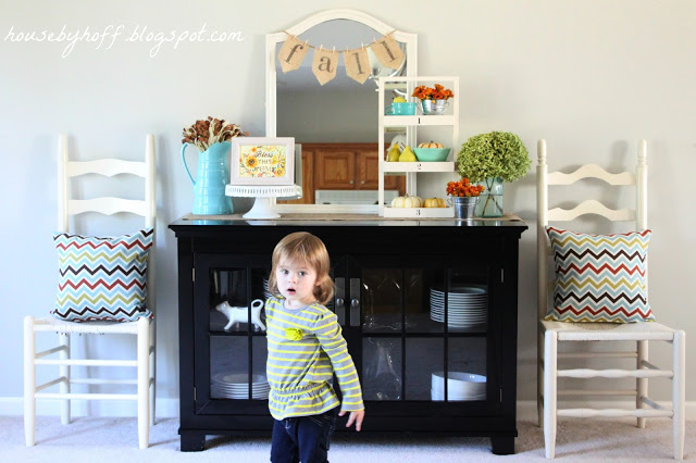 Little girl standing in front of the china cabinet and fall vignette.