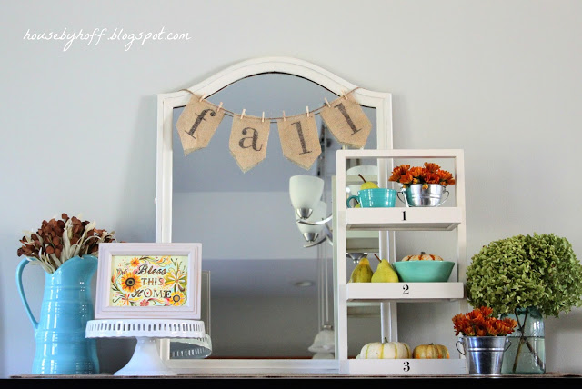 White mirror with fall strung across it and cake stand with frame on it and topiary.