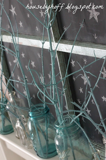 Clear blue mason jars with branches in them on the mantel.