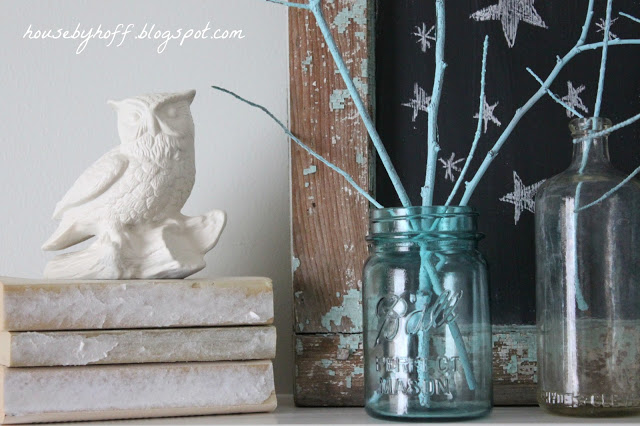 White owl figure sitting on antique books beside the glass mason jars on mantel.