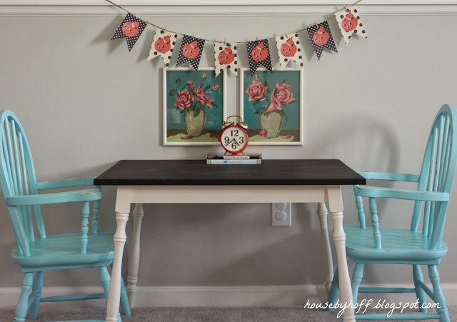 A table with blue chairs, and a pumpkin garland on the wall.