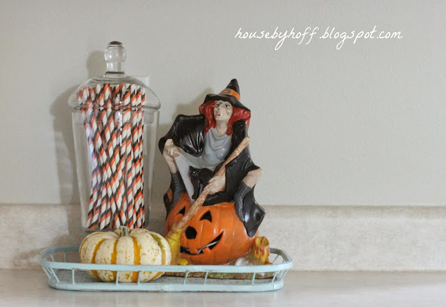 A witch sitting on a jack-o-lantern beside orange and black straws on the counter.