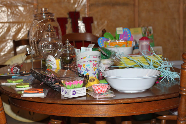 Wooden table filled with party planning items, paper cups, bowls, cupcake holders.