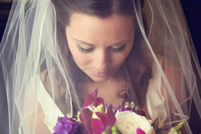 A bride with the veil covering her face looking at her bouquet.