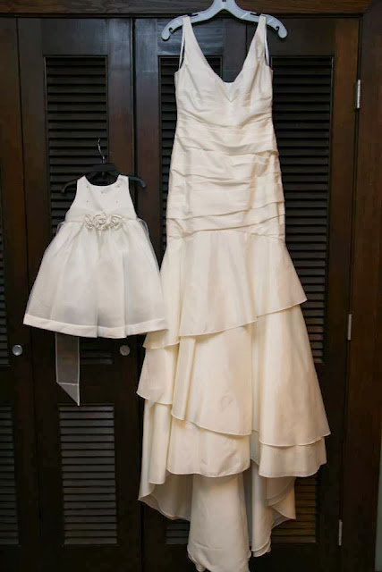 A white wedding dress and flower girl dress hanging by the closet.