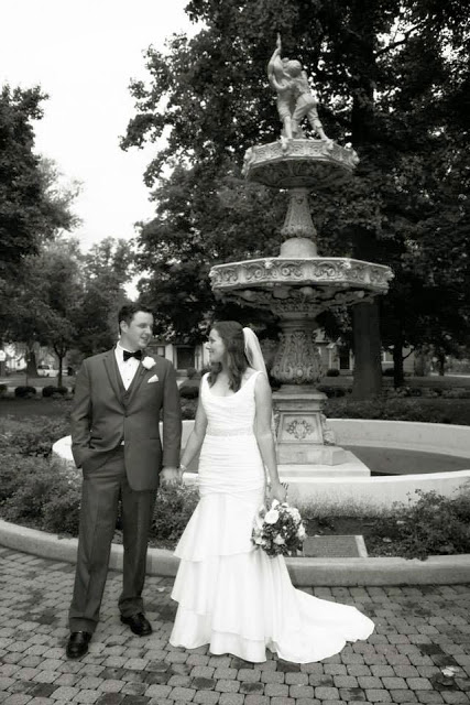 The bride and her husband in front of the fountain holding hands.