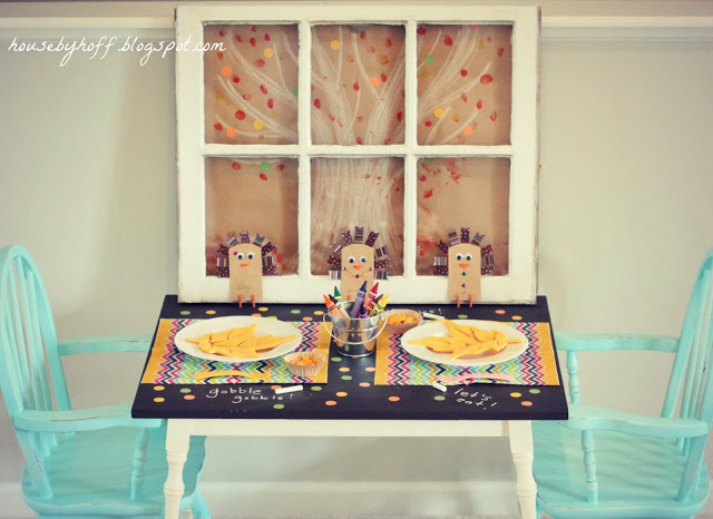 A window pane by the table with two light blue chairs.   The table decorated with crayons and colourful placemats.