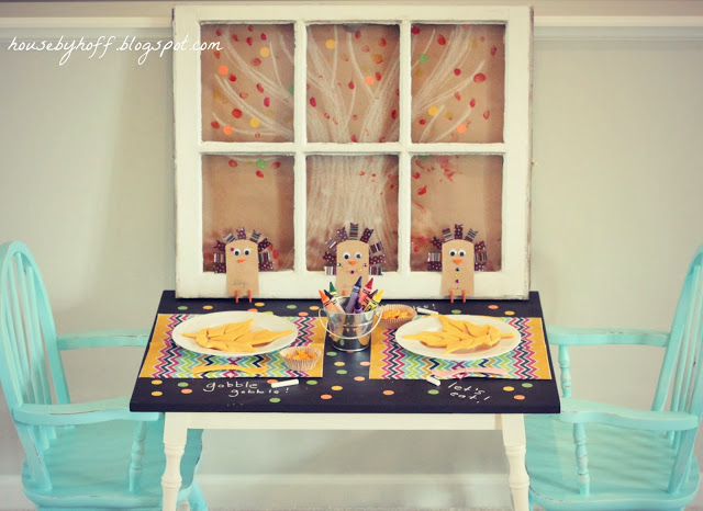 A window pane by the table with two light blue chairs. The table decorated with crayons and colourful placemats.