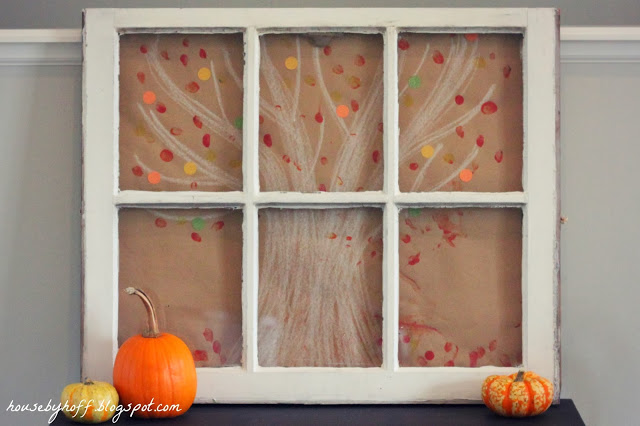 The artwork displayed on the mantel with small pumpkins beside it.