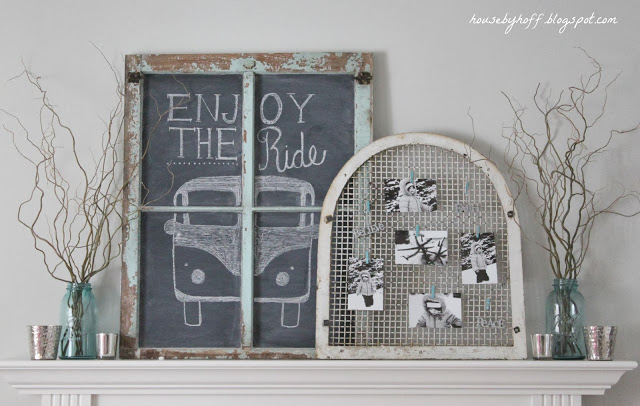 A white fireplace mantel with branches in glass jars and a an old window frame with pictures on it.