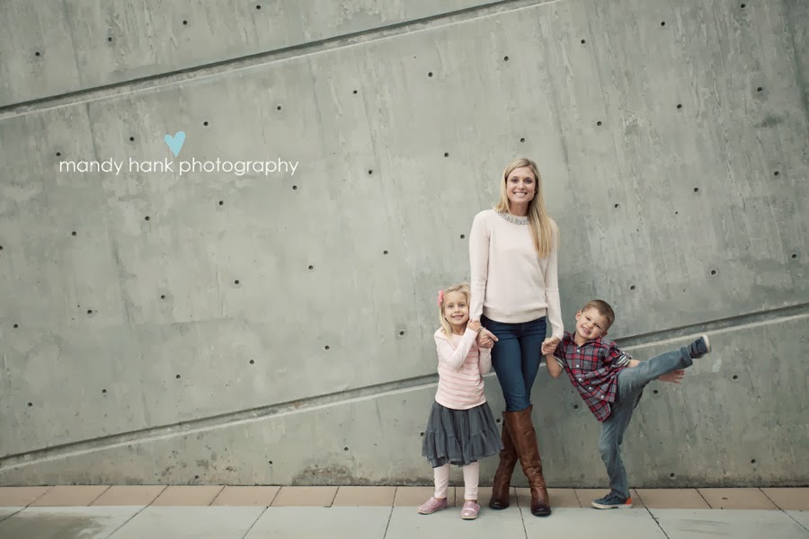 Portrait of a Mom and her kids against a concrete wall.