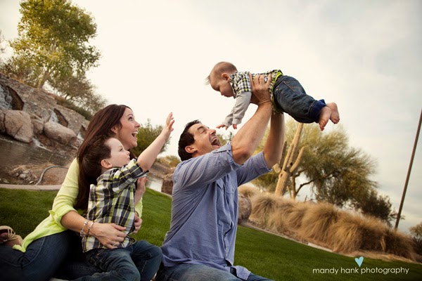 Dad holding a child up in his arms while the mom and other child look on.