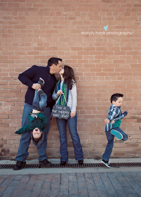 Mom and Dad kissing against a brick wall with the Dad holding a child upside down.