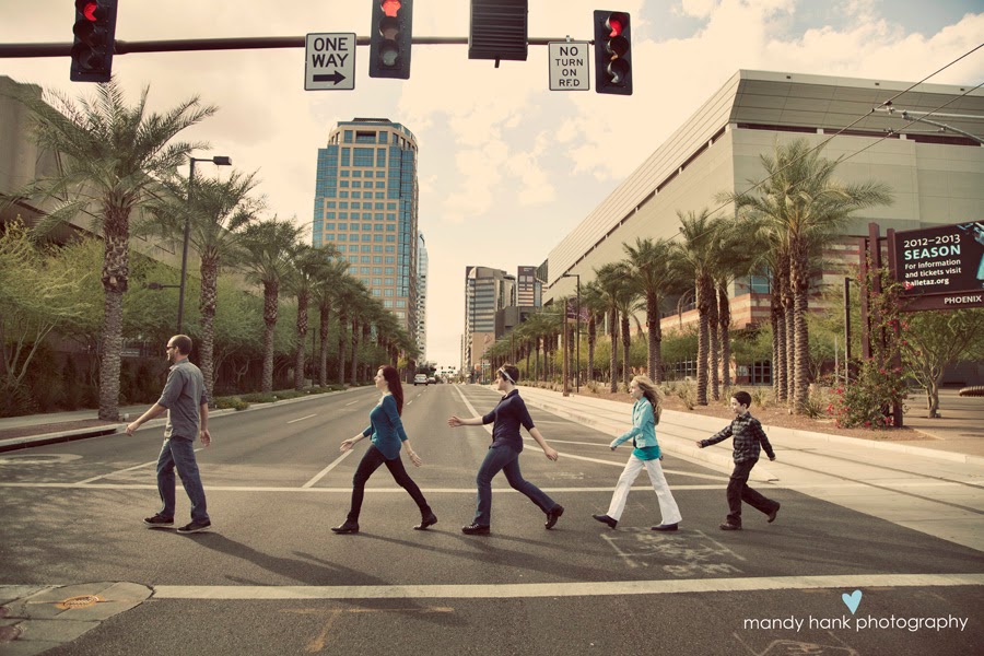 5 people walking across the street in a sidewalk in a line getting their picture taken.