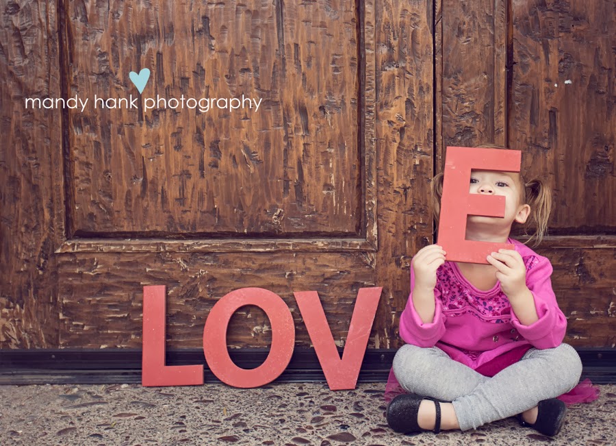 Little girl with a love sign and holding the E in front of her face.