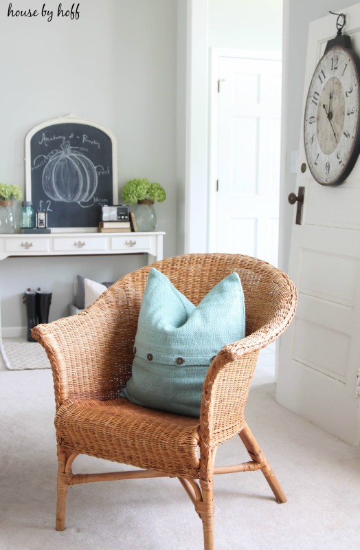 Wicker chair sitting in living room with chalkboard on table in the back.