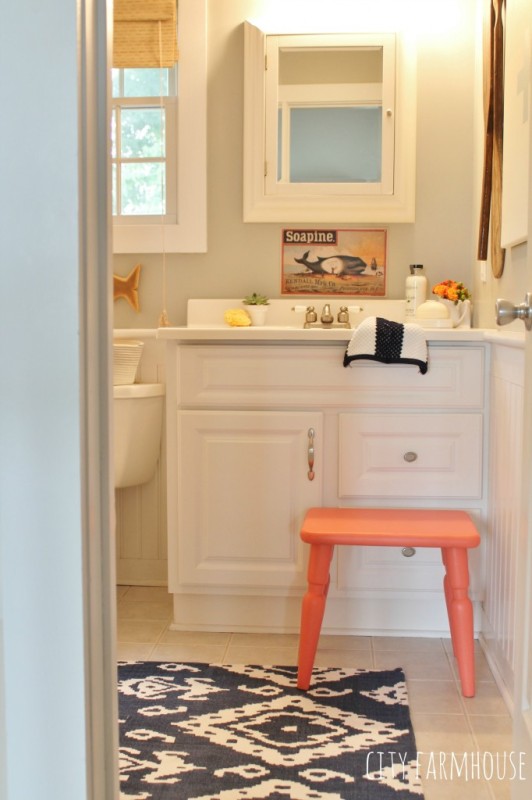 Blue and white rug with orange stool in a neutral bathroom.