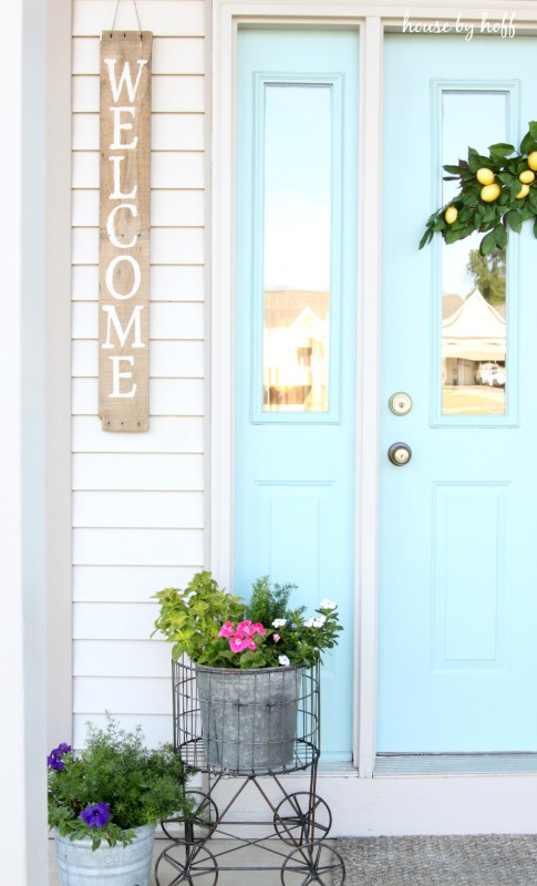 Light blue door, and flowers plus the welcome sign hanging outside.