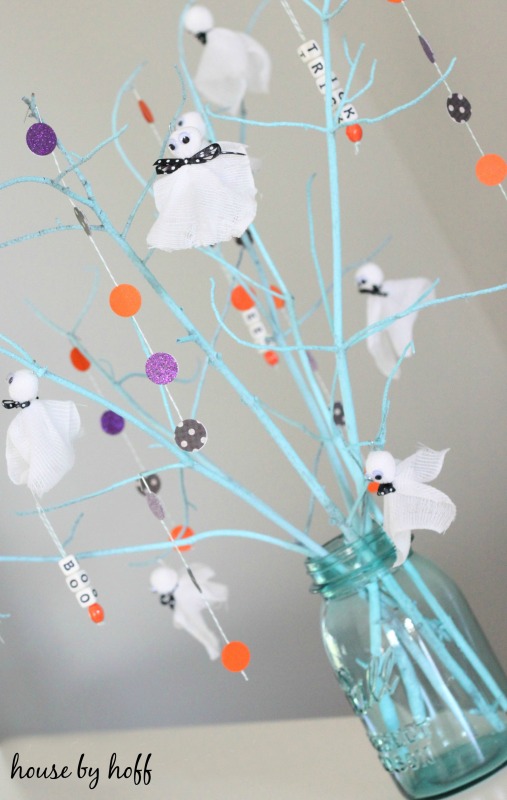Light blue mason jar with homemade ghosts on branches.