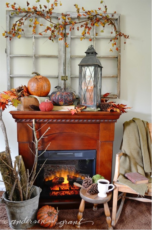 Fireplace that is on with pumpkins and lanterns on mantel.