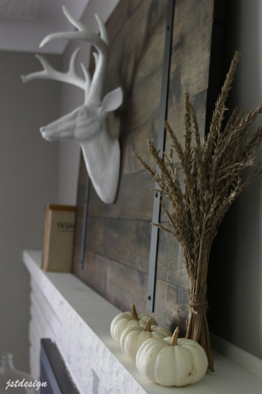 A barn door with a faux deer head in white porcelain on it, beside white pumpkins on the fireplace mantel.