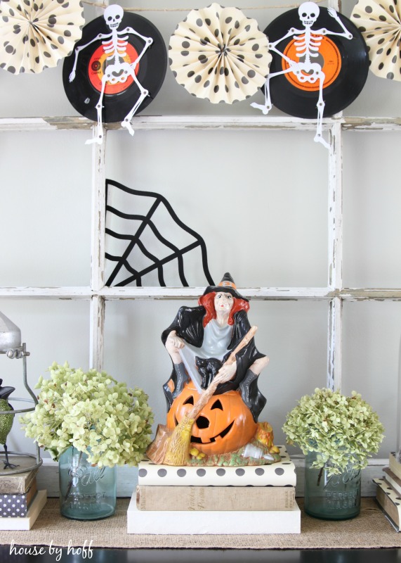 Table top with witch sitting on a pumpkin and skeletons and black spiders web.