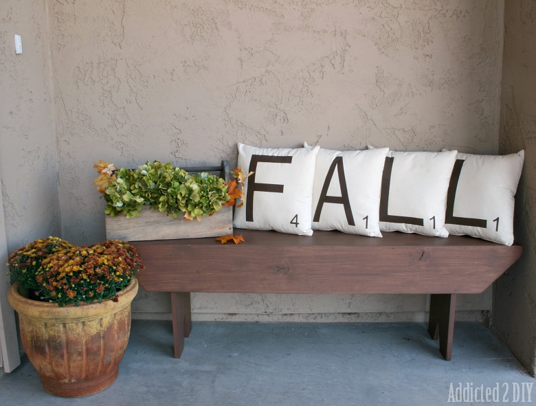 A wooden bench with four pillows all spelling out the word FALL.