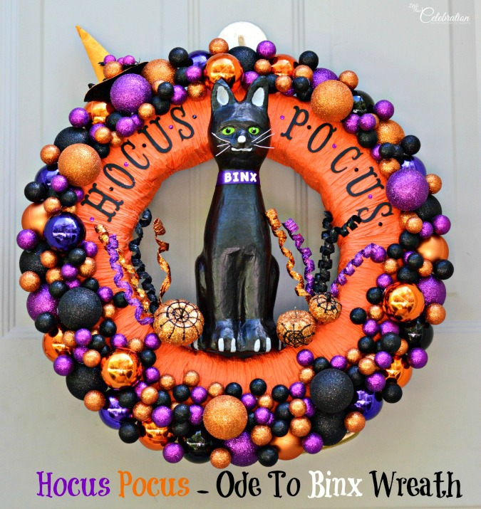 A bright orange with purple, black and gold wreath that says hocus pocus.   A large Binx cat is in the middle of the wreath.