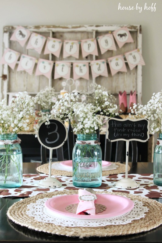 Table setting with pink plates and mason jars filled with white flowers on table.