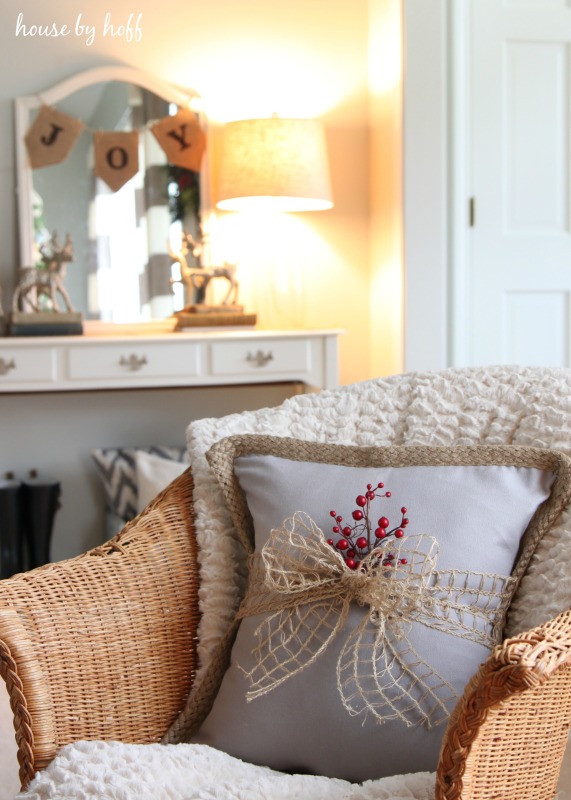 A neutral coloured bow tied around a pillow with a sprig of red berries.