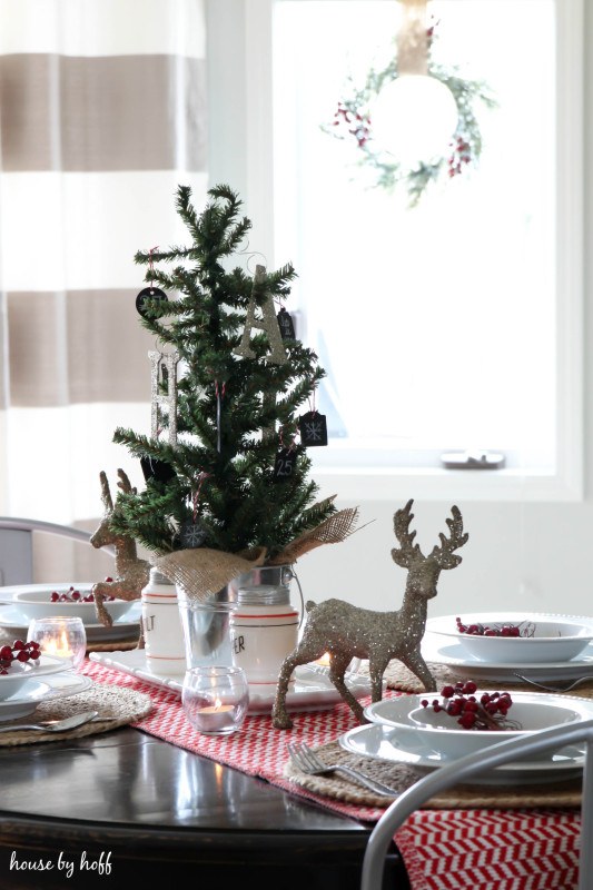 There is a sparkly deer on the table with white plates and a red and white table runner.