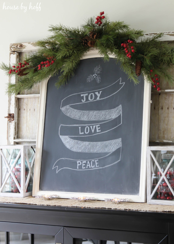 A chalkboard with Joy Love and Peace written on it, plus a garland of holly on the top of the board.