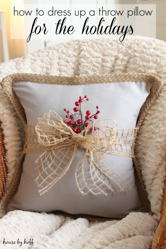 A cozy armchair with a pillow that has a bow and some red berries around it.