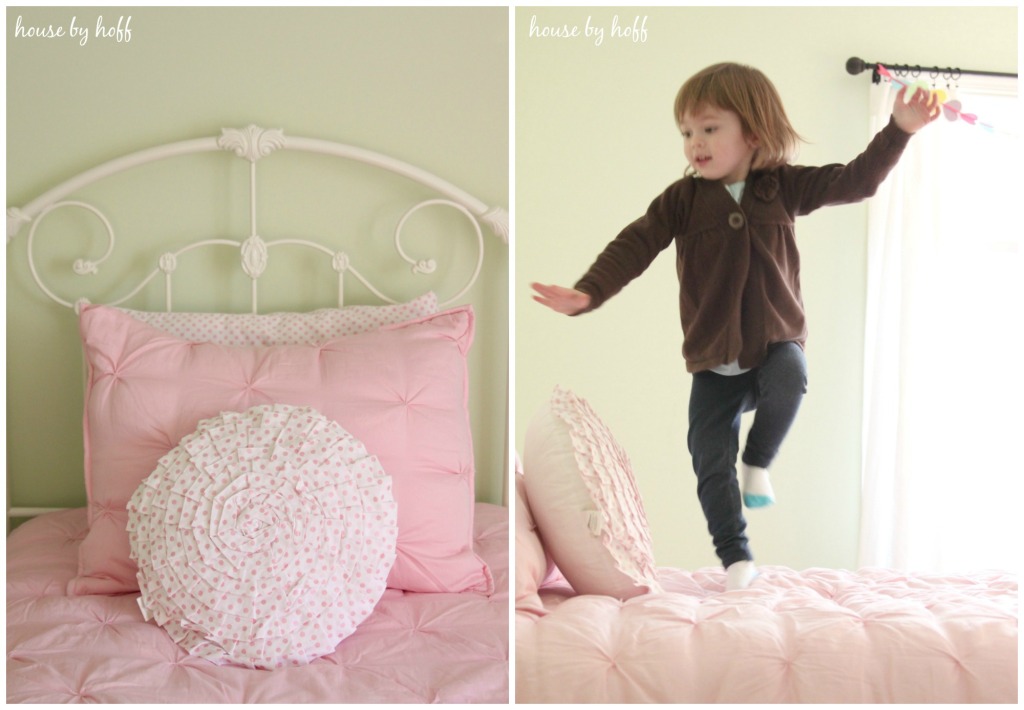 White bed frame, pink blanket and pink pillows and little girl jumping on the bed.