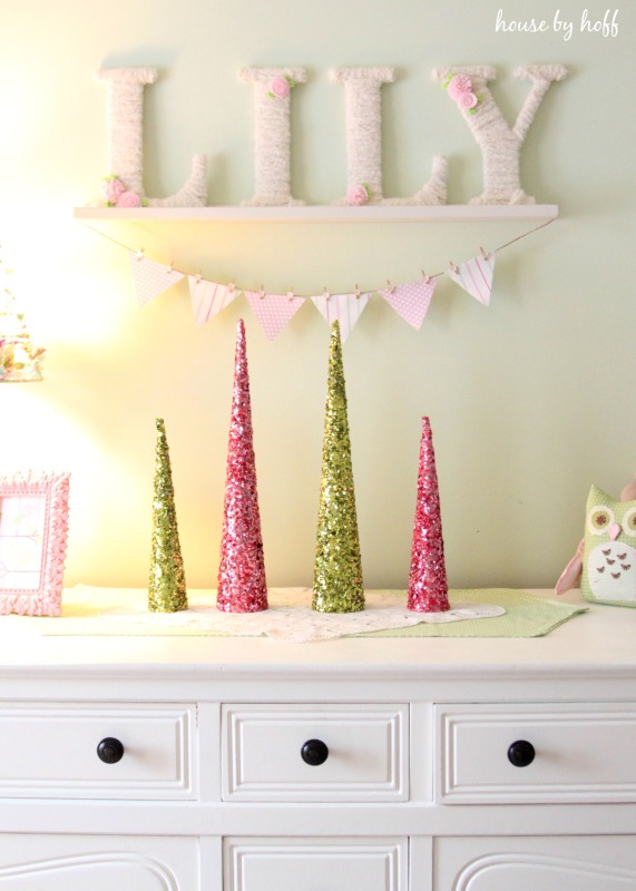 Small sparkly Christmas trees are on the dresser in pink and green.
