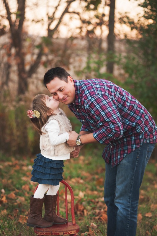 Little girl standing on a chair kissing Dad's cheek.