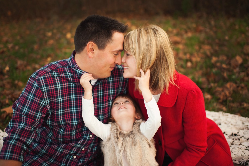 A couple looking at each other with a child reaching up to them in a portrait picture.