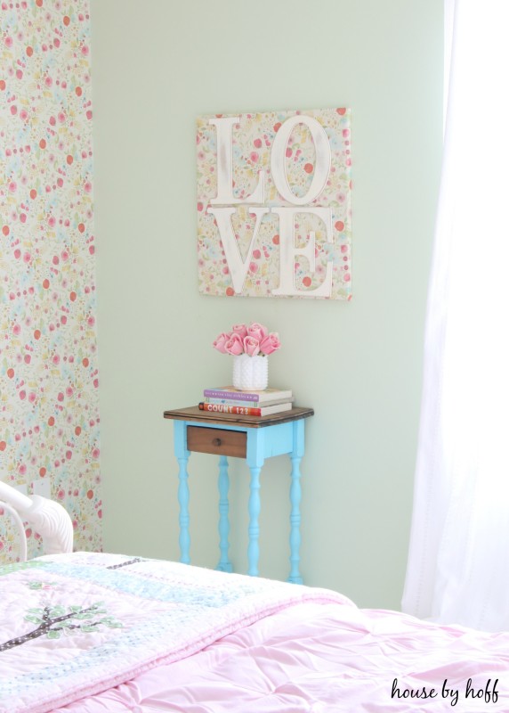 Little side table with pink flowers on it and love on a poster picture hanging on the wall.