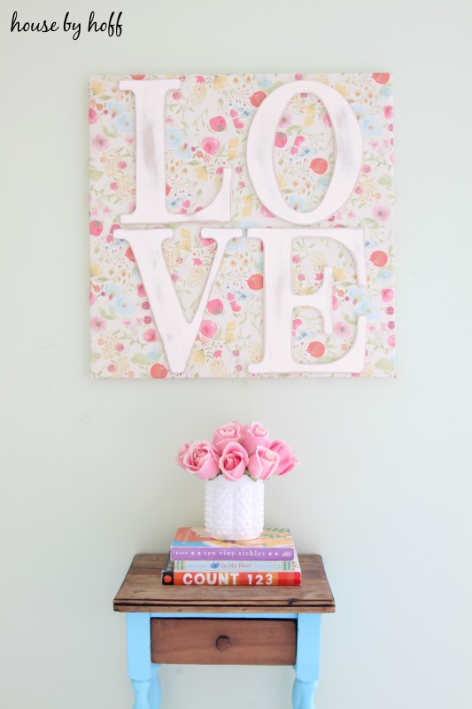 The wall art, a side table with pink roses in a vase under the art.