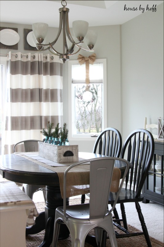 A round wooden dining room table, and striped curtains in the dining room.