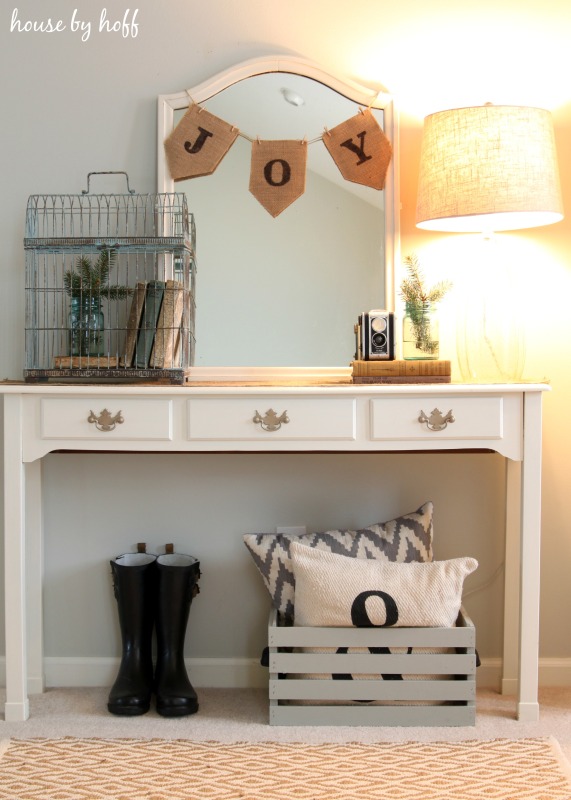 A hallway table with a mirror on it and a joy banner.