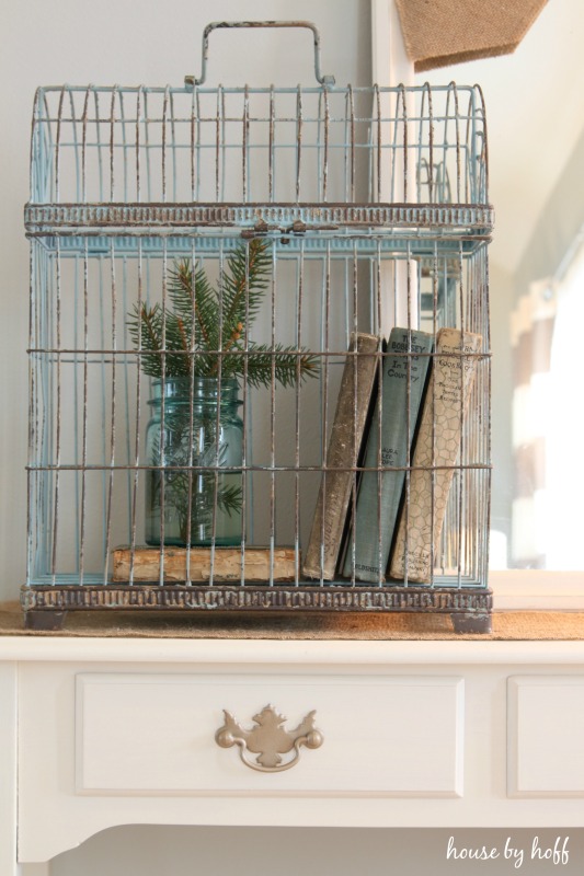 A birdcage filled with antique books, and evergreen clippings.