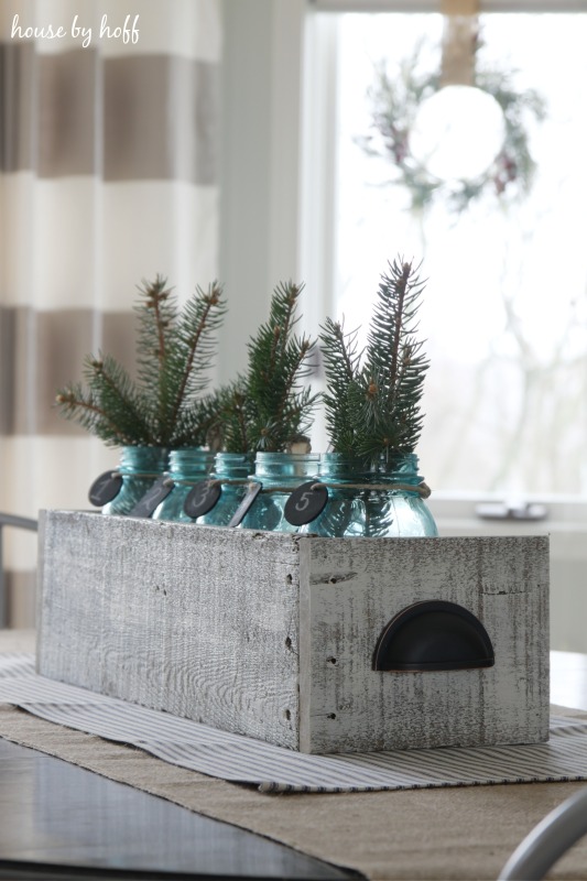 Five mason jars filled with evergreen clippings on the middle of the table.