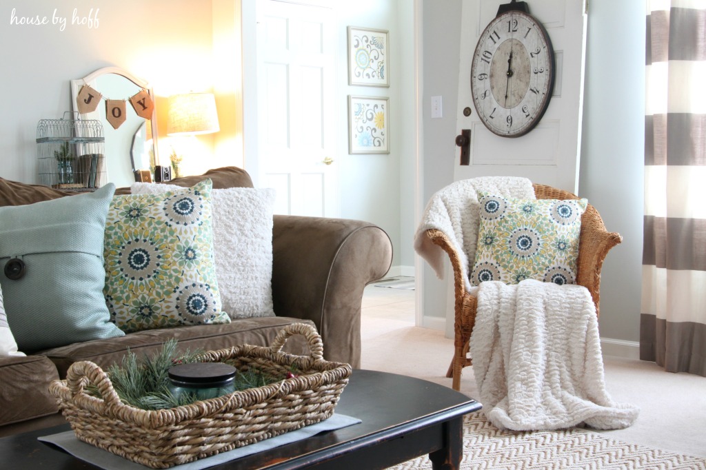 A brown couch, wicker chair both with floral pillows on it.