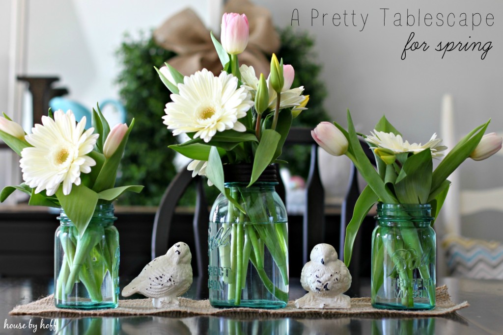 Mason jars filled with white flowers and birds in between the jars on the table.